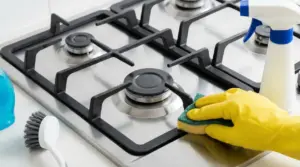 Pulizia di un fornello a gas con guanto di gomma e spugna su piano cottura in acciaio