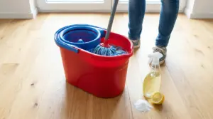 Secchio per la pulizia con mocio, spray, limone e bicarbonato su pavimento in legno