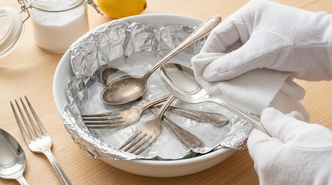 Posate d'argento annerite immerse in una ciotola con alluminio durante la pulizia naturale