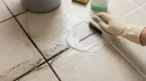 Una mano con guanto pulisce lo sporco tra le fughe delle piastrelle del pavimento con una spazzola