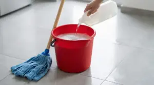 Secchio rosso con acqua saponata e mocio su un pavimento chiaro