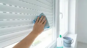Una mano pulisce una tapparella con un panno in microfibra vicino a una finestra.