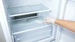 Mano con guanto che pulisce il foro di scarico in un frigorifero con una spazzola