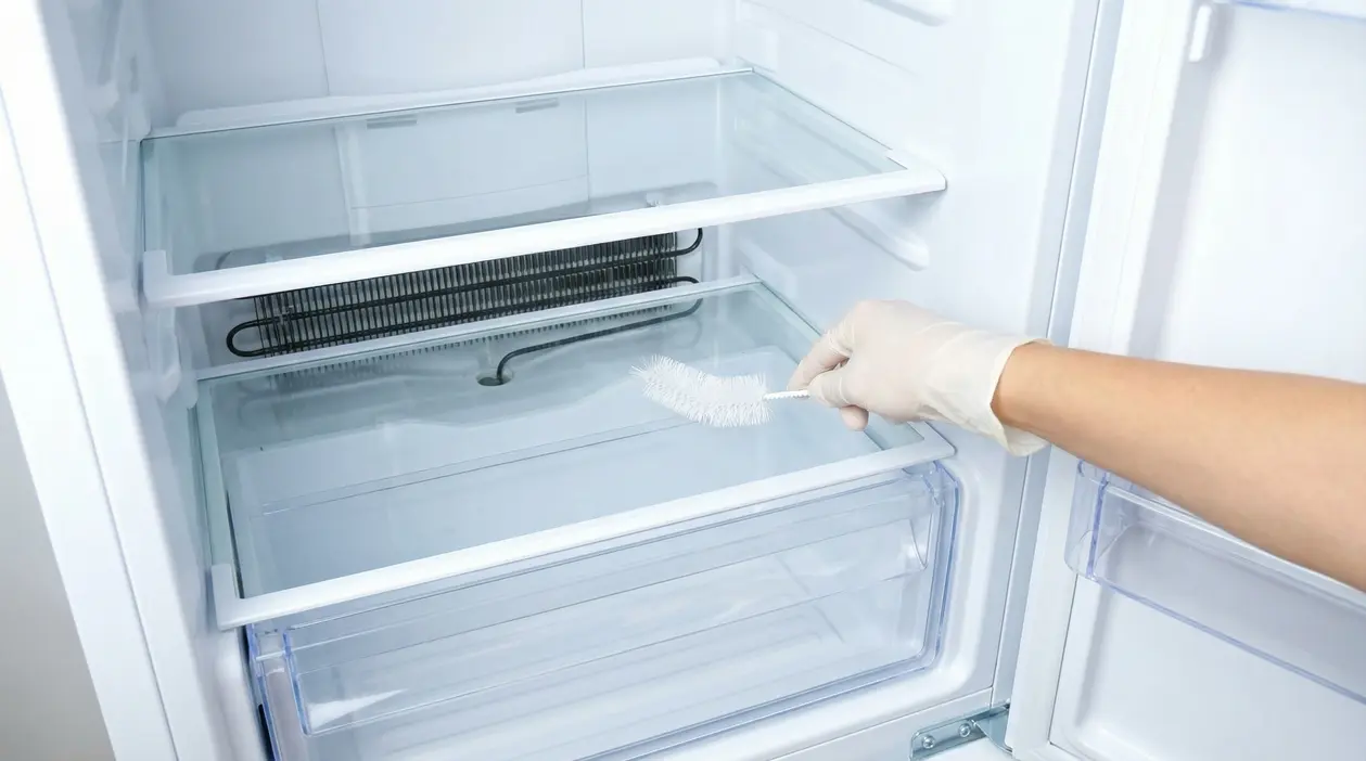 Mano con guanto che pulisce il foro di scarico in un frigorifero con una spazzola