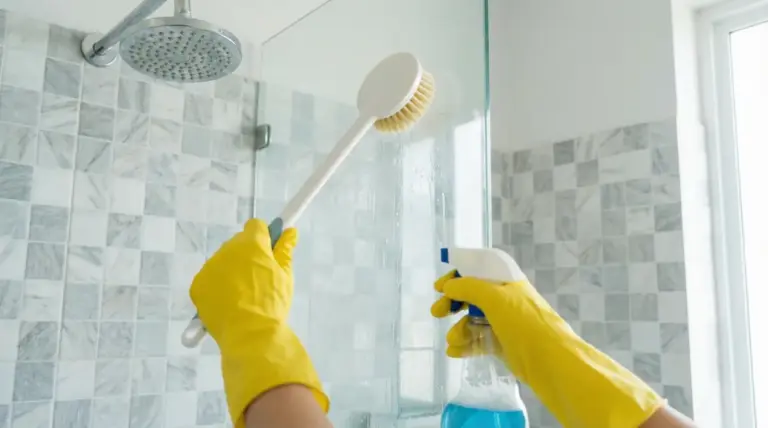 Persona con guanti gialli pulisce il box doccia con spazzola e detergente