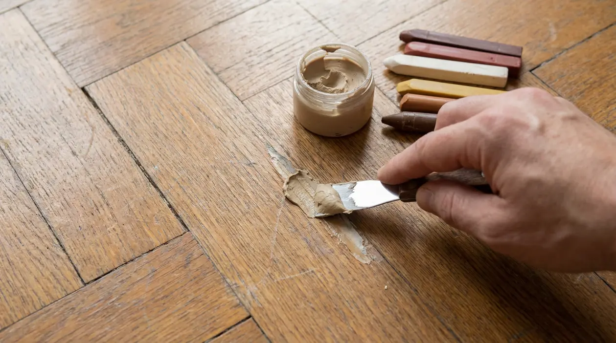 Riparazione di un graffio su parquet con stucco e spatola
